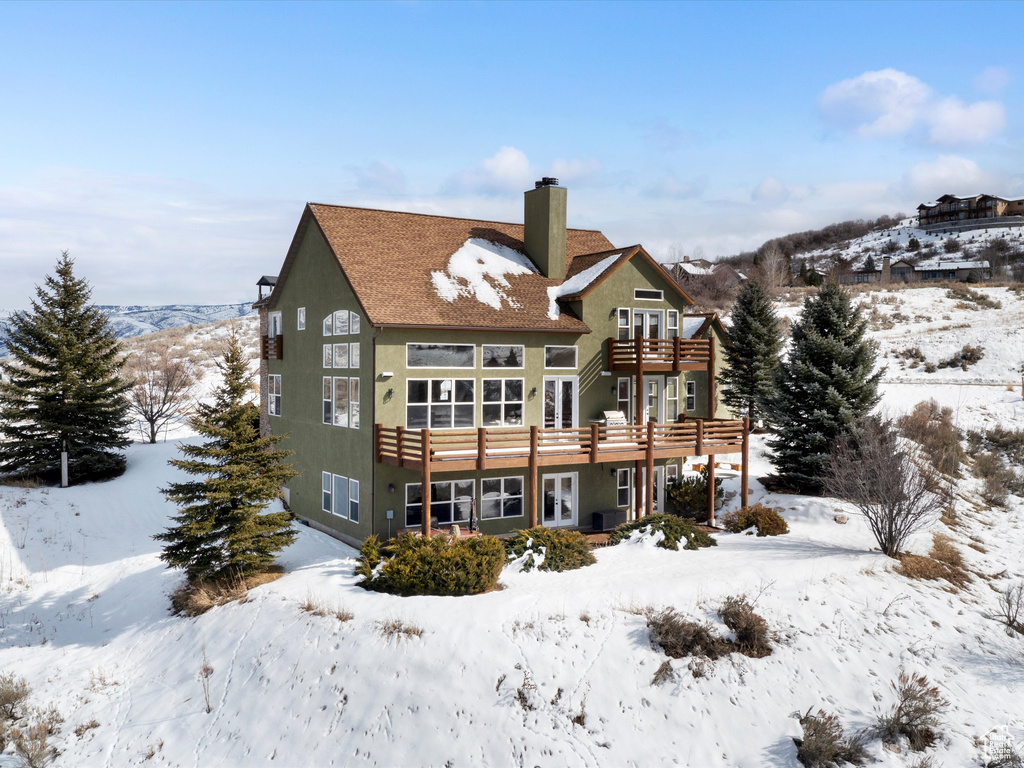 Snow covered house featuring a chimney and a balcony