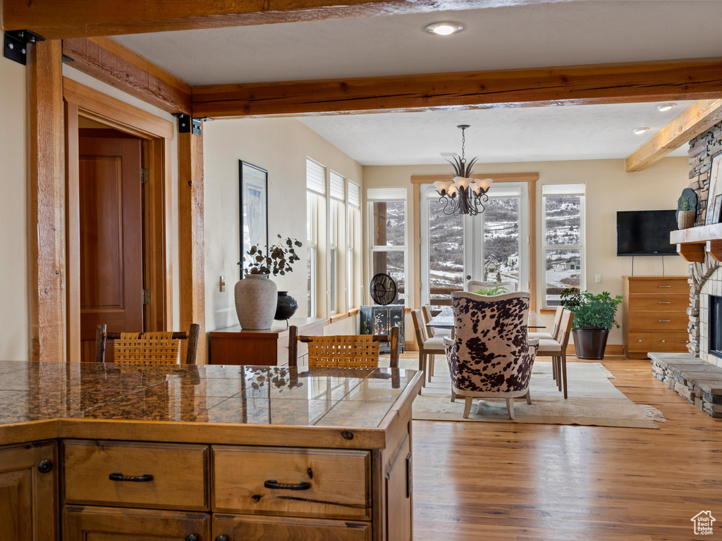 Kitchen featuring beam ceiling, a fireplace, tile countertops, hanging light fixtures, and brown cabinetry