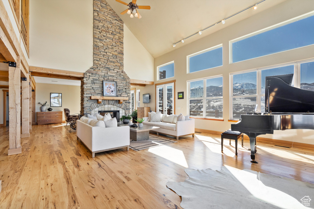 Living room with ceiling fan, high vaulted ceiling, a fireplace, wood finished floors, and track lighting