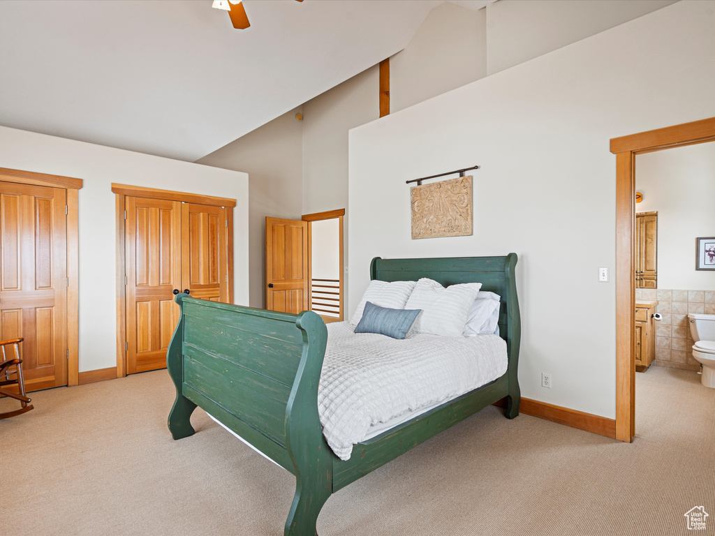 Bedroom with light carpet, baseboards, high vaulted ceiling, and ensuite bathroom