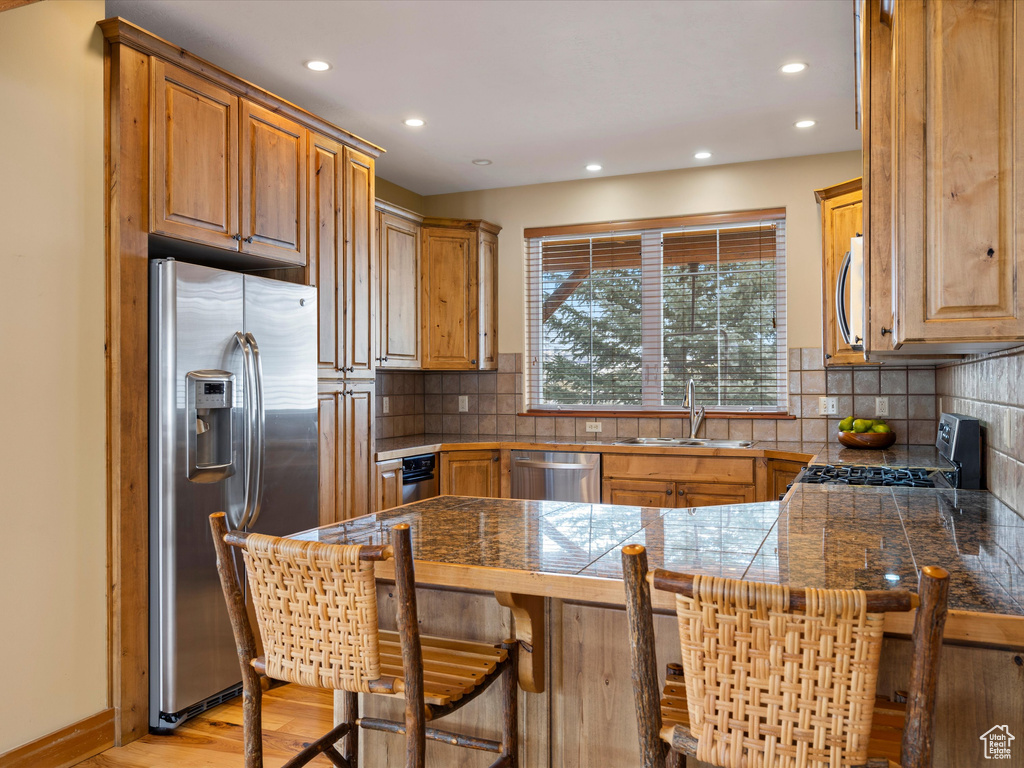 Kitchen with tile countertops, a peninsula, a breakfast bar, a sink, and appliances with stainless steel finishes