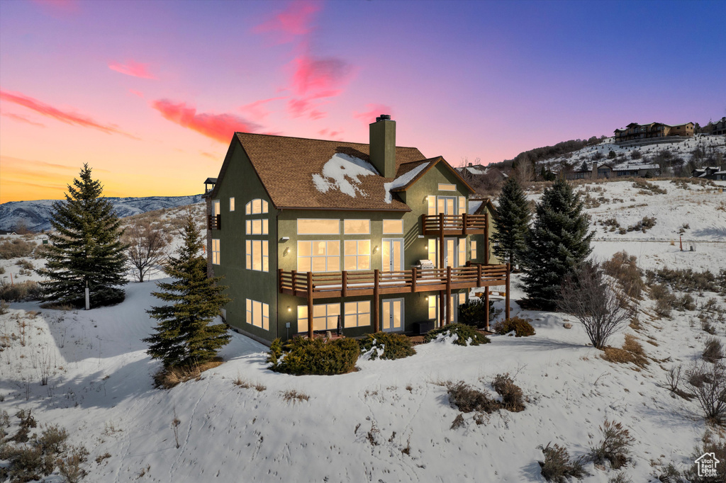 Snow covered house with a chimney, a balcony, and stucco siding