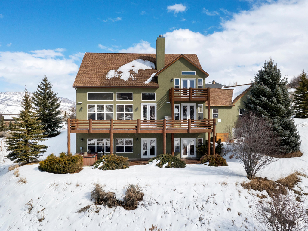 Snow covered property with french doors, a chimney, and a wooden deck