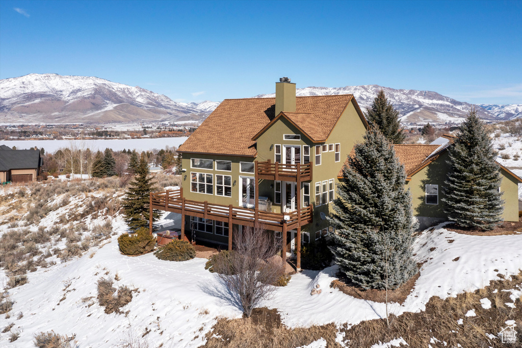 Snow covered back of property with a deck with mountain view, a chimney, a balcony, and stucco siding