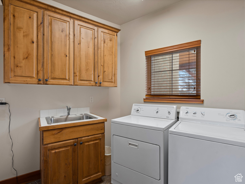 Clothes washing area featuring washer and clothes dryer, a sink, and cabinet space