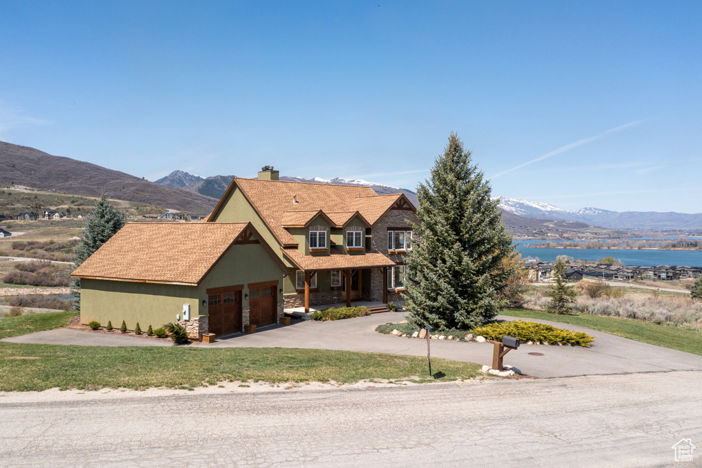View of front facade with a front lawn, a garage, a water and mountain view, a chimney, and concrete driveway