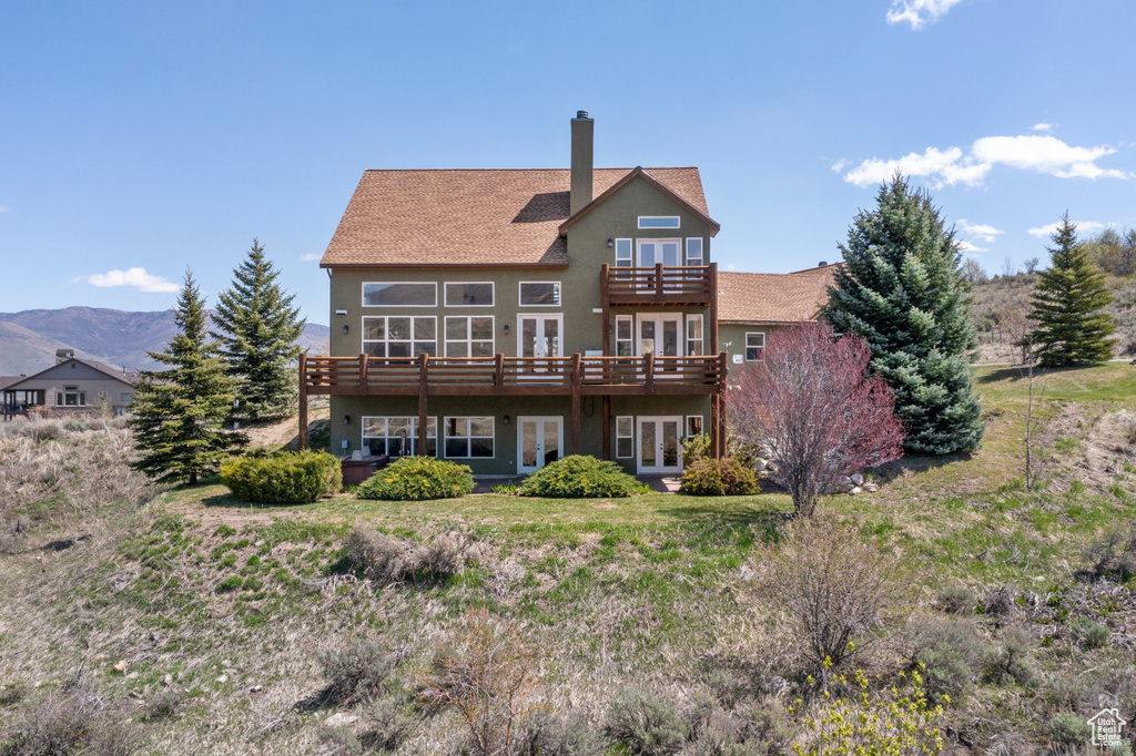 Back of property featuring a balcony, a chimney, stucco siding, a deck with mountain view, and french doors