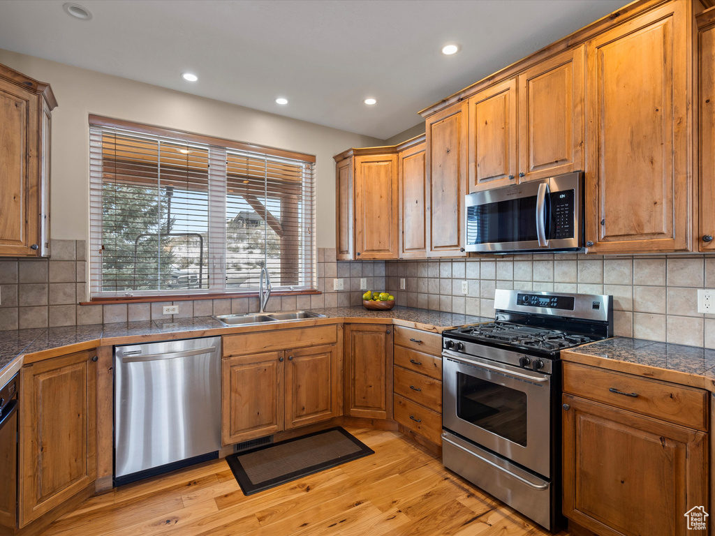 Kitchen featuring stainless steel appliances, brown cabinetry, a sink, and tile countertops