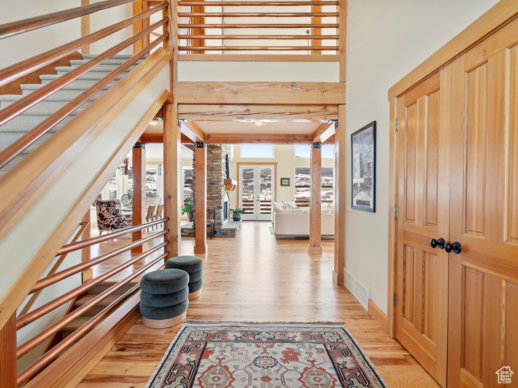 Entryway with light wood finished floors, baseboards, a high ceiling, beamed ceiling, and ornate columns