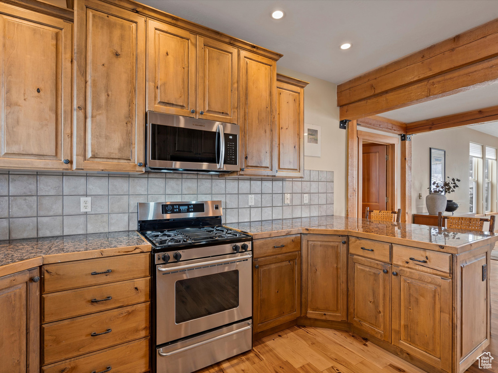 Kitchen with appliances with stainless steel finishes, brown cabinetry, light wood-style flooring, and a peninsula