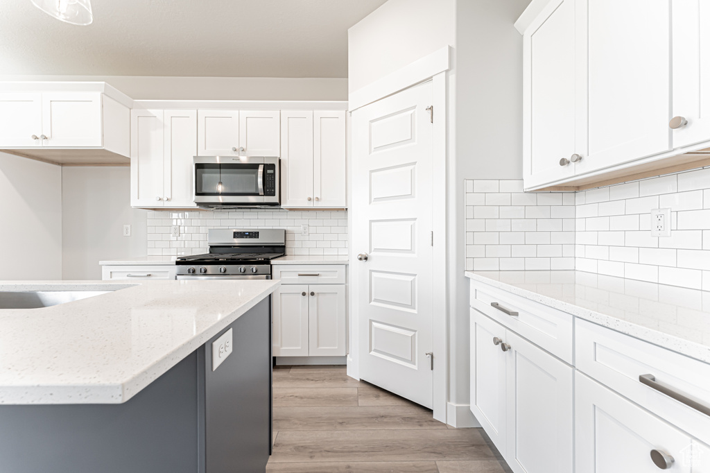 Kitchen featuring appliances with stainless steel finishes, white cabinets, light wood-type flooring, and backsplash
