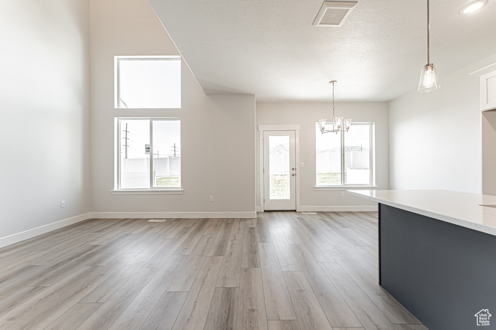 Unfurnished dining area featuring a chandelier, light wood-style floors, baseboards, and a textured ceiling