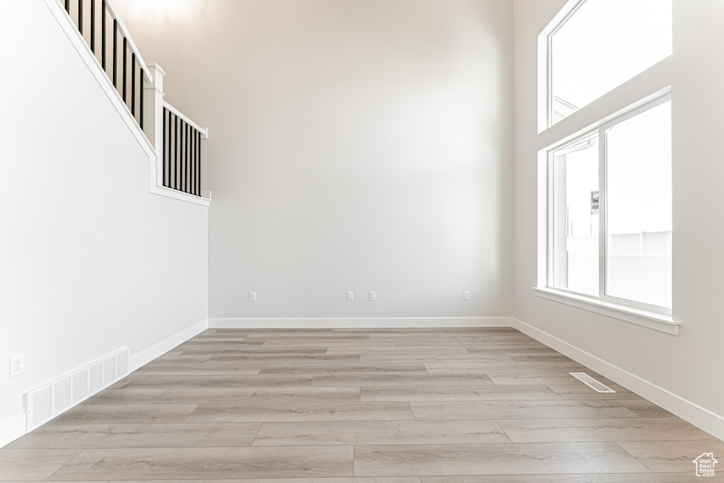 Spare room featuring light wood-type flooring, baseboards, and a towering ceiling