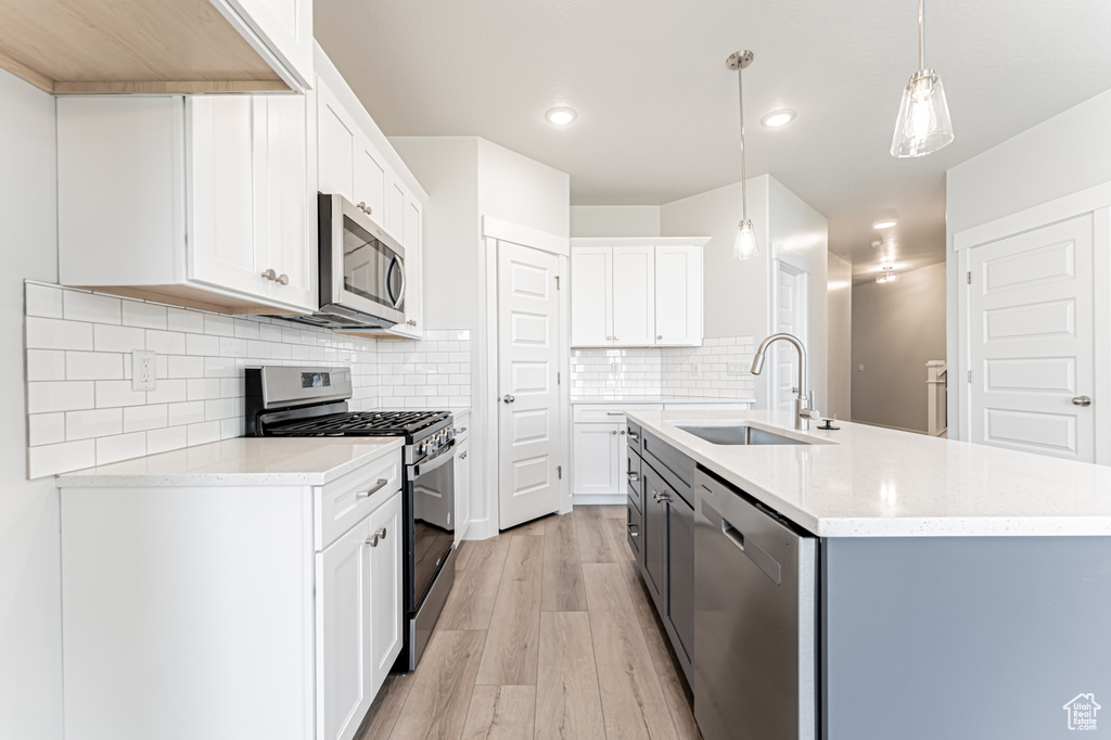 Kitchen with stainless steel appliances, light wood-style flooring, a sink, an island with sink, and decorative light fixtures