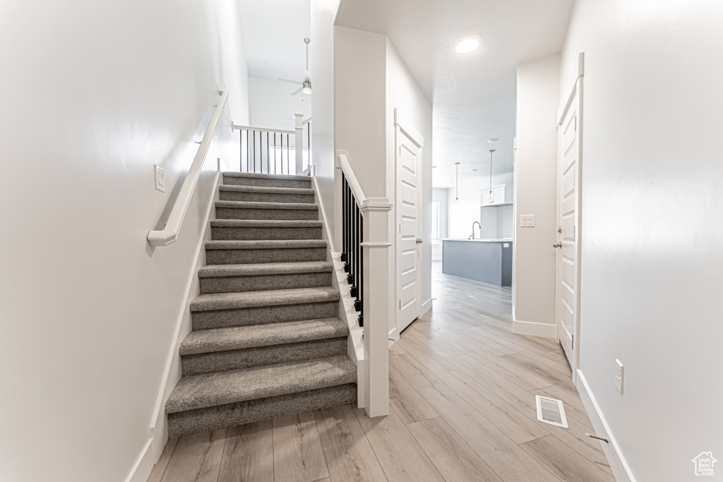 Stairs with ceiling fan, wood finished floors, and baseboards