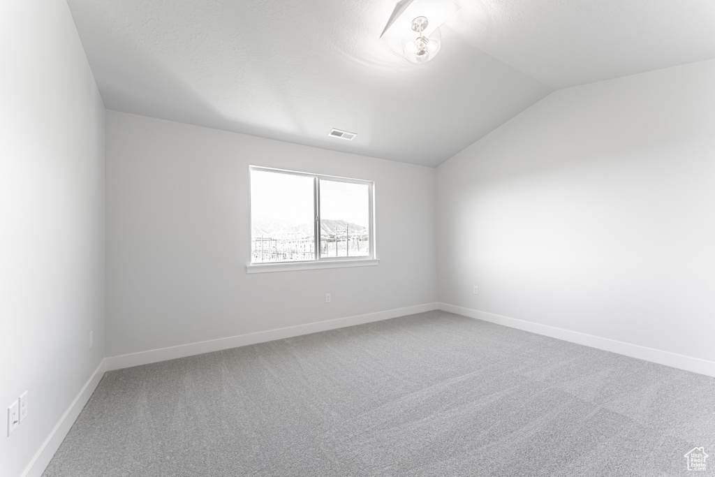 Carpeted empty room featuring vaulted ceiling and baseboards