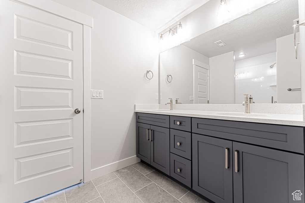 Bathroom with double vanity, tile patterned flooring, baseboards, and a textured ceiling