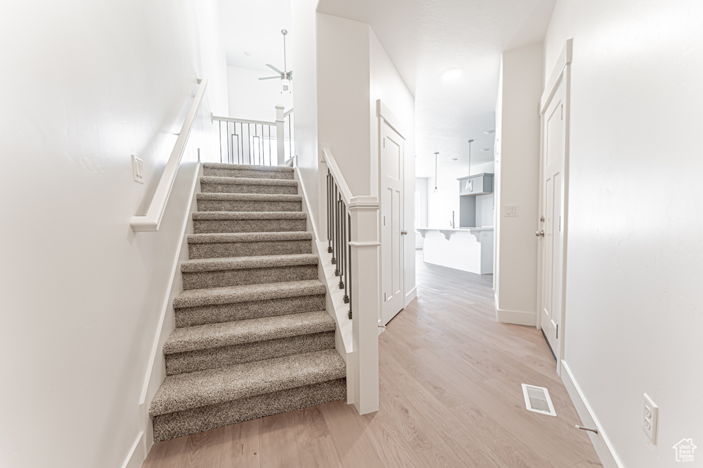 Stairway with wood finished floors, ceiling fan, and baseboards