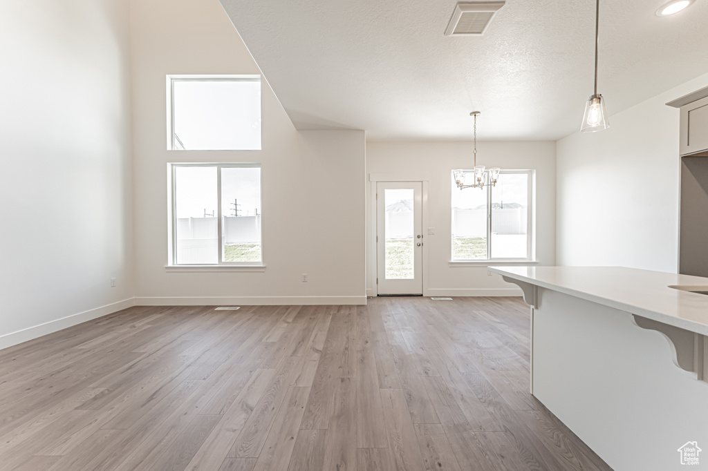 Unfurnished living room with a chandelier, light wood-style floors, and baseboards