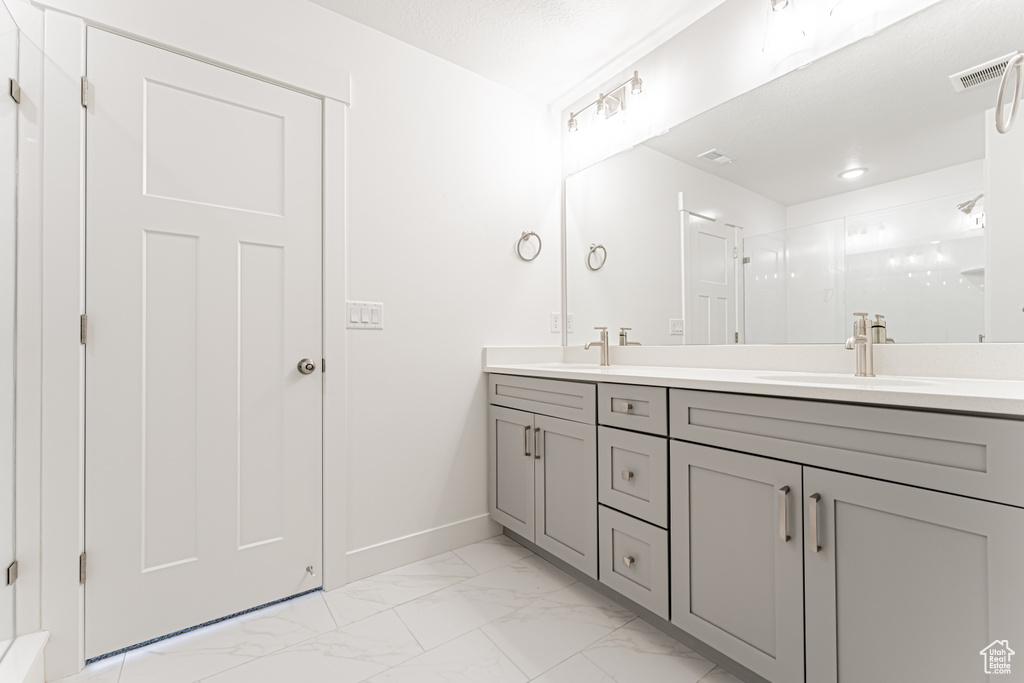 Bathroom with double vanity, marble finish floors, baseboards, and a shower with shower door