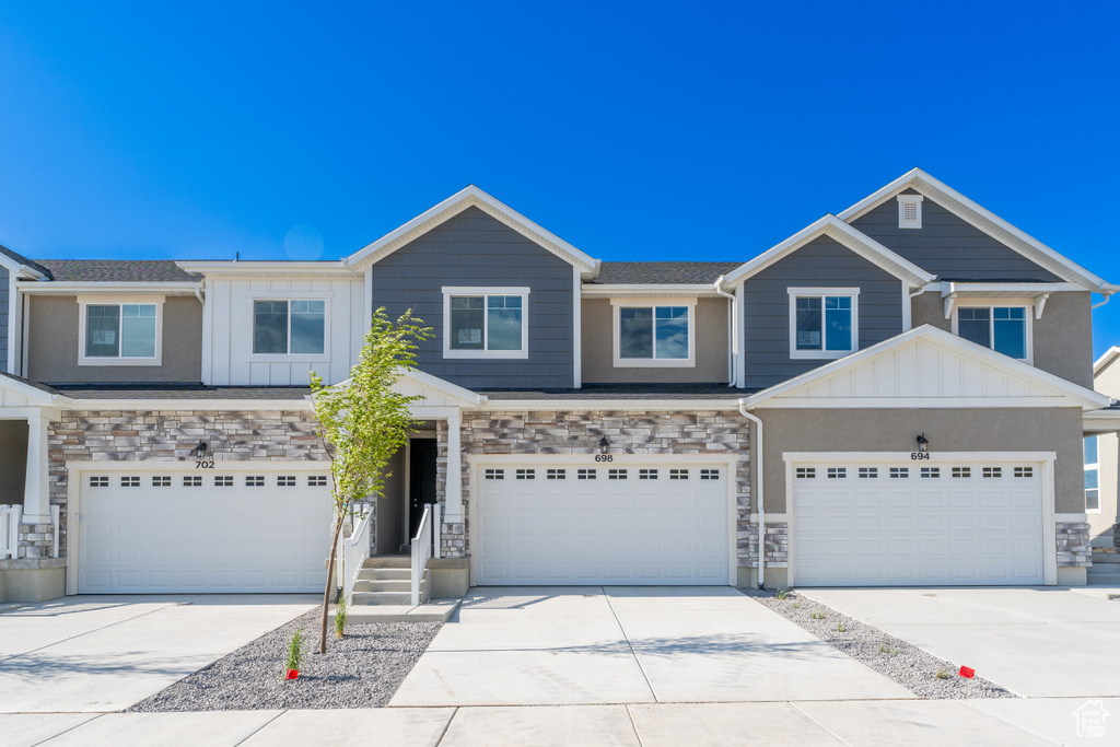 Townhome / multi-family property with concrete driveway, an attached garage, board and batten siding, and stone siding
