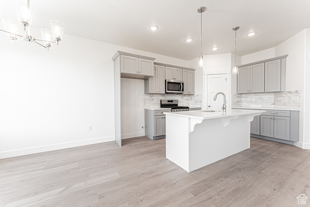 Kitchen featuring gray cabinetry, appliances with stainless steel finishes, a sink, decorative backsplash, and a breakfast bar area