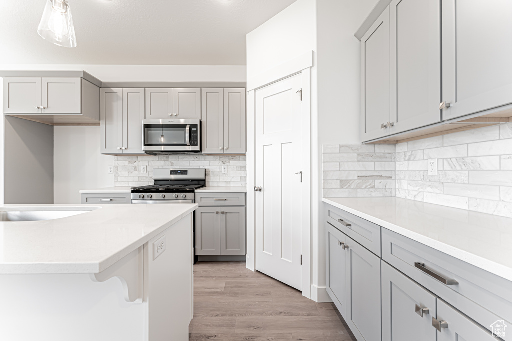 Kitchen with stainless steel appliances, gray cabinetry, light wood-style floors, decorative backsplash, and light countertops