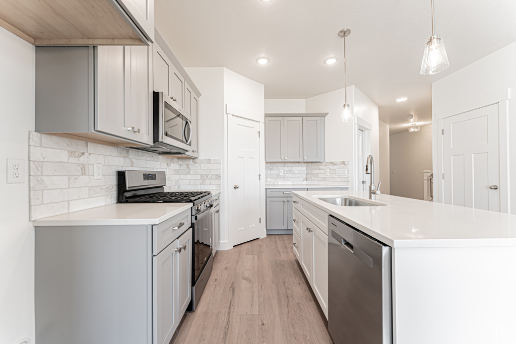 Kitchen with stainless steel appliances, a sink, light wood-type flooring, light countertops, and gray cabinets