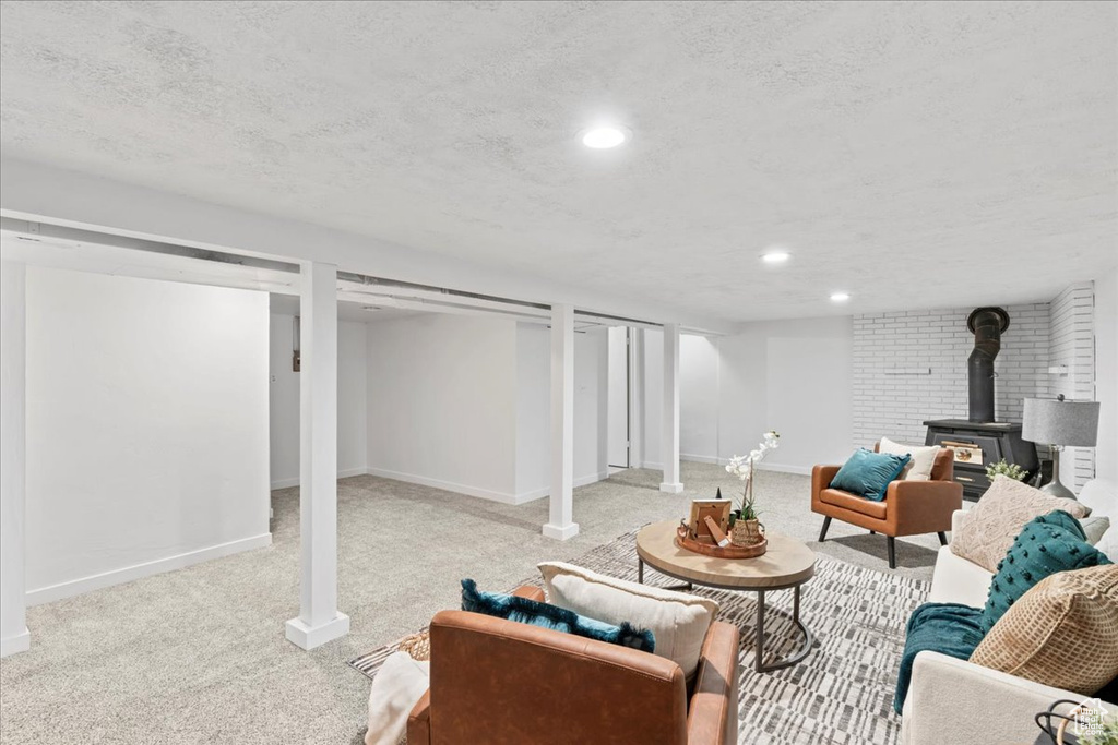 Finished below grade area with carpet floors, a textured ceiling, baseboards, a wood stove, and recessed lighting