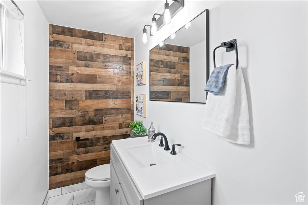 Bathroom with toilet, marble finish floor, wooden walls, and vanity