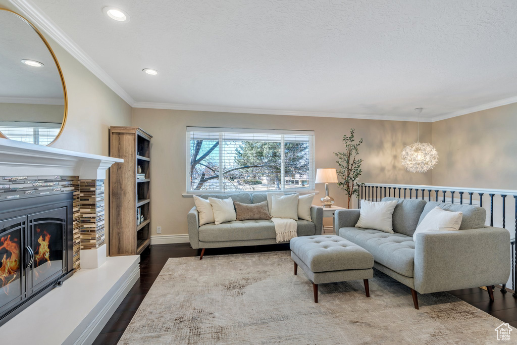 Living room with dark wood-style floors, a glass covered fireplace, crown molding, and baseboards