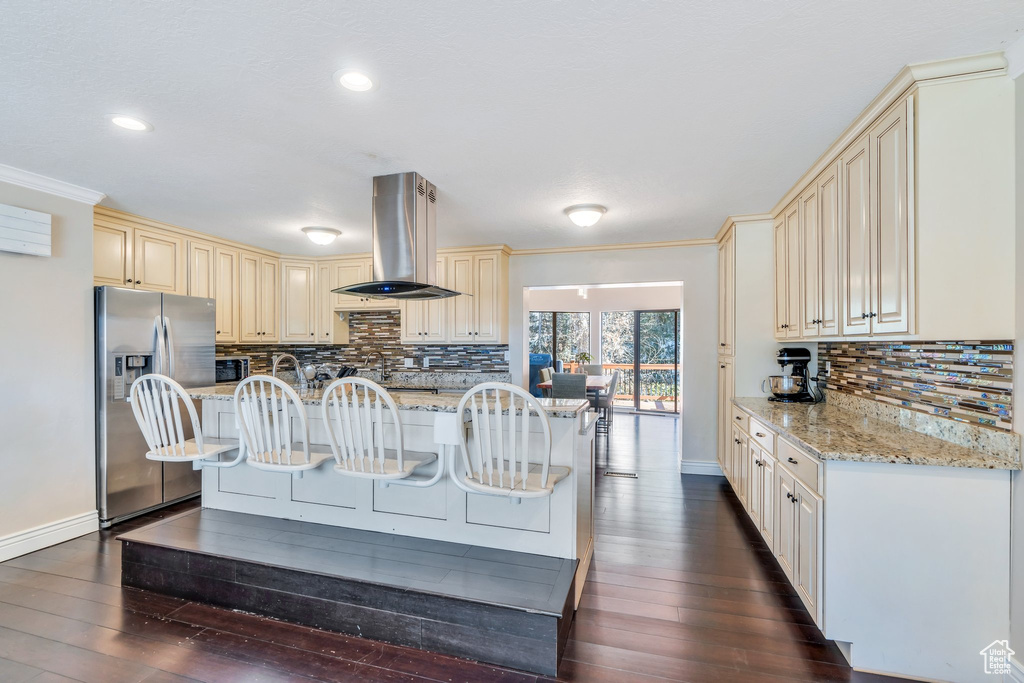 Kitchen with a kitchen bar, island exhaust hood, light stone counters, and stainless steel fridge with ice dispenser