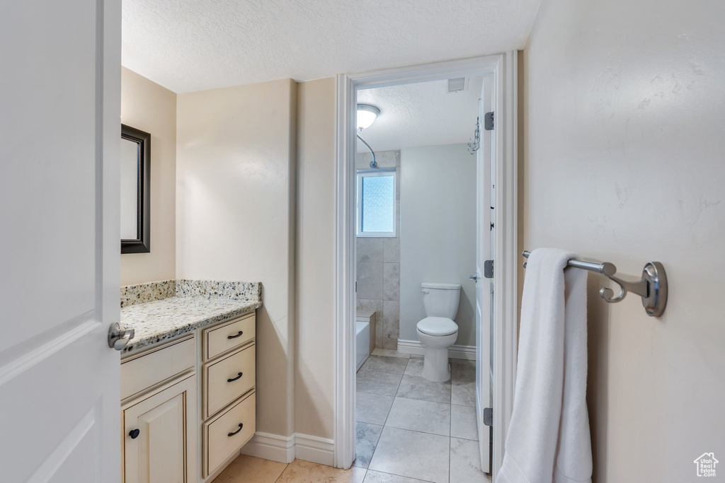 Full bathroom with bathtub / shower combination, toilet, vanity, a textured ceiling, and baseboards