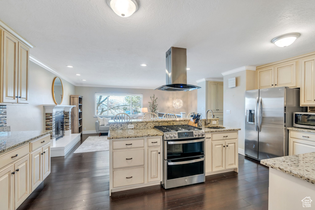 Kitchen featuring stainless steel appliances, cream cabinets, island exhaust hood, and light stone countertops