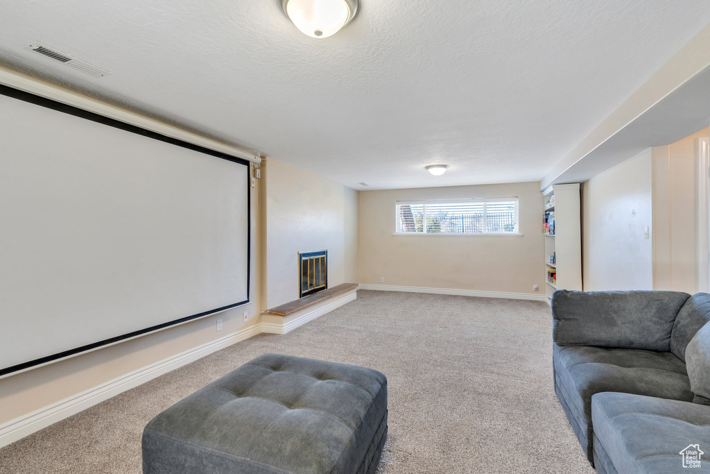 Home theater featuring a large fireplace, baseboards, visible vents, light colored carpet, and a textured ceiling