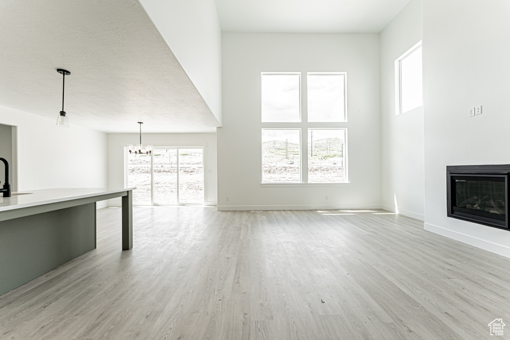 Unfurnished living room with a chandelier, a glass covered fireplace, light wood-style floors, a towering ceiling, and baseboards