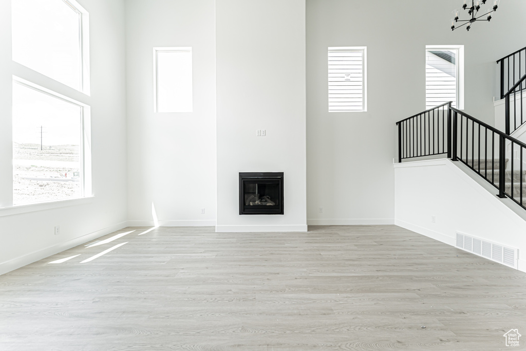 Unfurnished living room featuring stairs, wood finished floors, a high ceiling, baseboards, and a glass covered fireplace