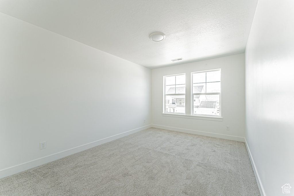 Empty room featuring light colored carpet, baseboards, and a textured ceiling