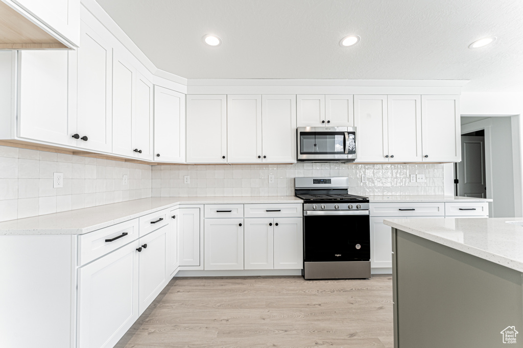 Kitchen featuring stainless steel appliances, white cabinetry, light wood finished floors, tasteful backsplash, and recessed lighting