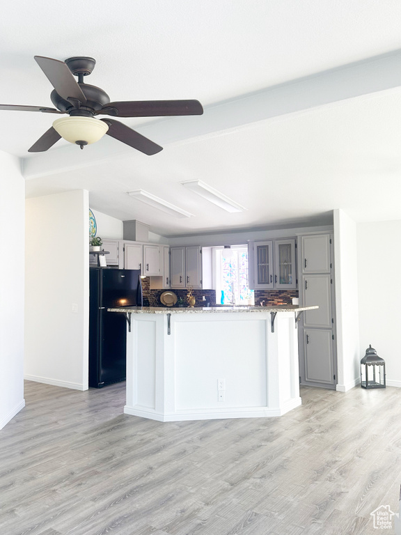 Kitchen featuring vaulted ceiling, gray cabinets, a kitchen bar, and freestanding refrigerator