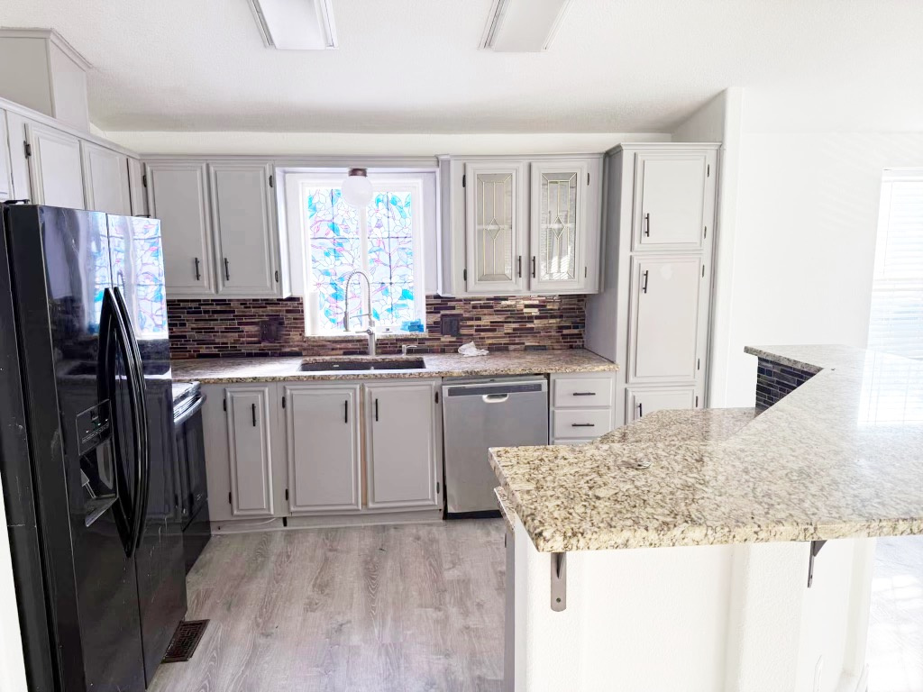 Kitchen featuring light wood-style flooring, a sink, stainless steel dishwasher, black fridge, and backsplash