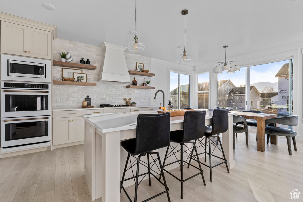 Kitchen with white double oven, light countertops, custom exhaust hood, built in microwave, and open shelves