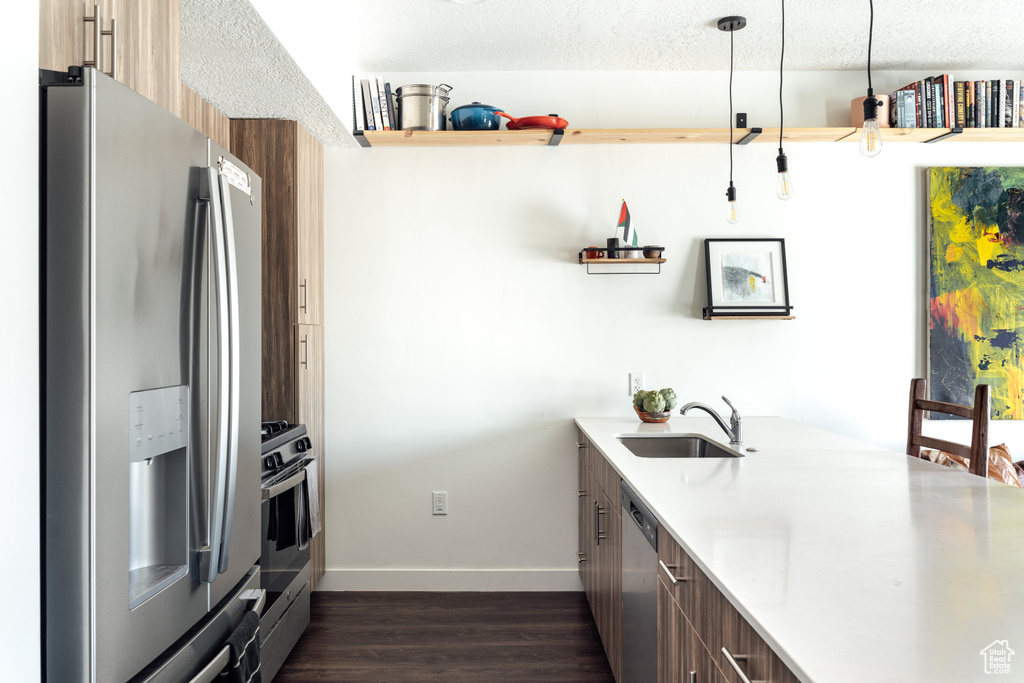 Kitchen with dark wood-style floors, decorative light fixtures, light countertops, appliances with stainless steel finishes, and a sink