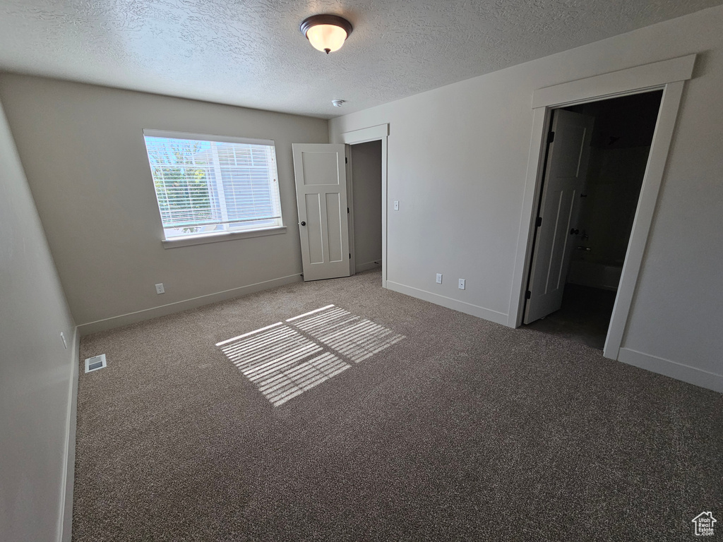 Unfurnished bedroom with a textured ceiling, carpet flooring, visible vents, and baseboards