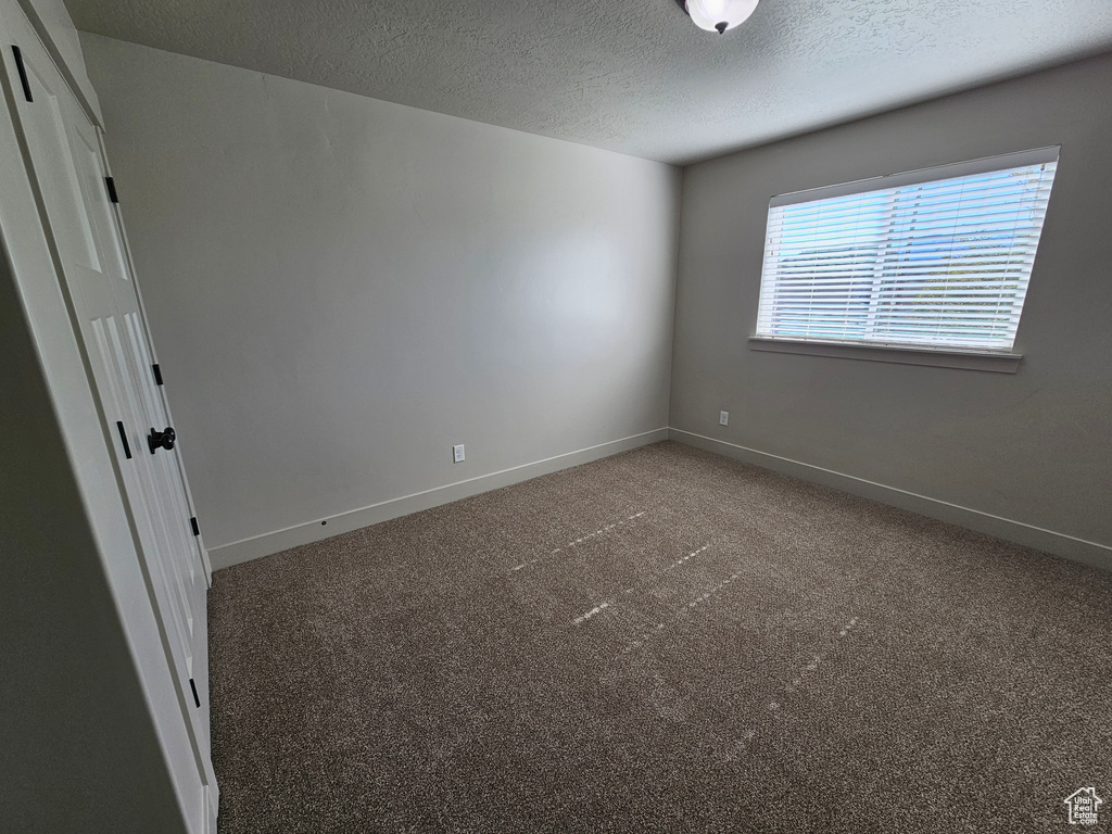 Carpeted spare room featuring a textured ceiling and baseboards