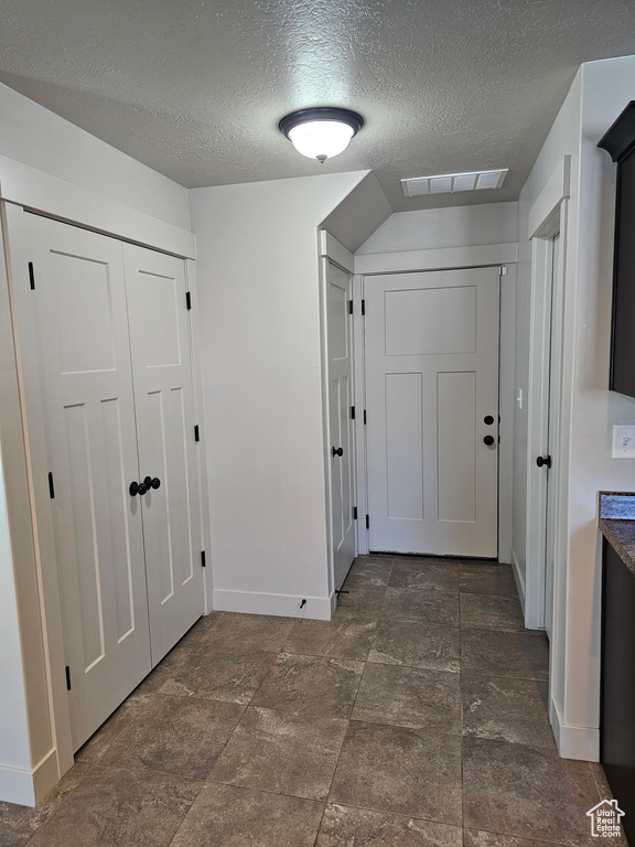 Corridor with a textured ceiling, stone finish floor, visible vents, and baseboards