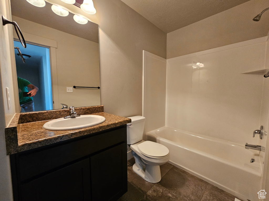 Bathroom with a textured ceiling, bathing tub / shower combination, vanity, and toilet