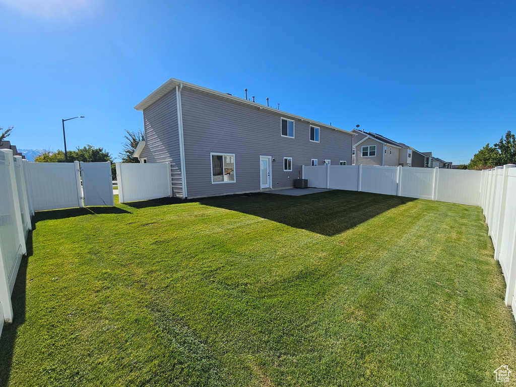 Back of house featuring a fenced backyard, central AC, and a lawn