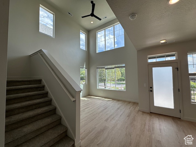 Entryway with ceiling fan, light wood finished floors, healthy amount of natural light, stairs, and a towering ceiling