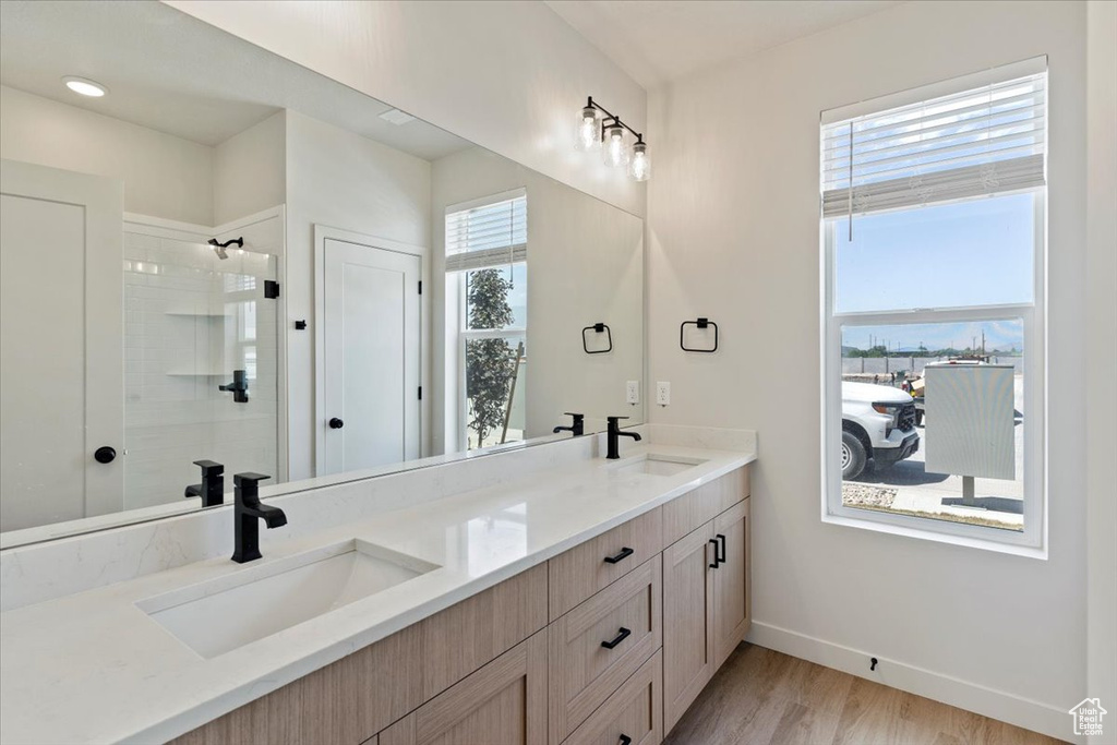 Bathroom featuring healthy amount of natural light, double vanity, tiled shower, and wood finished floors
